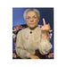 Elderly woman in vintage blouse sitting on floral chair with a serious expression and raised middle finger gesture.