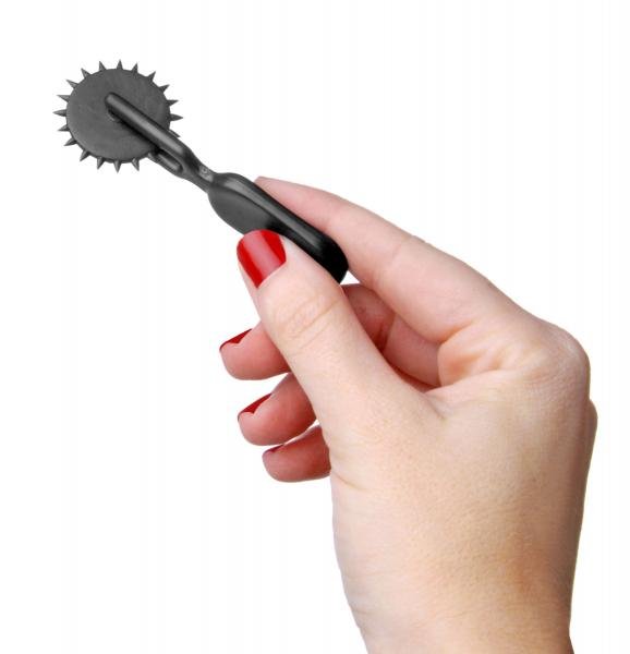 Hand holding a compact black sensation wheel with sharp spikes for tactile stimulation.
