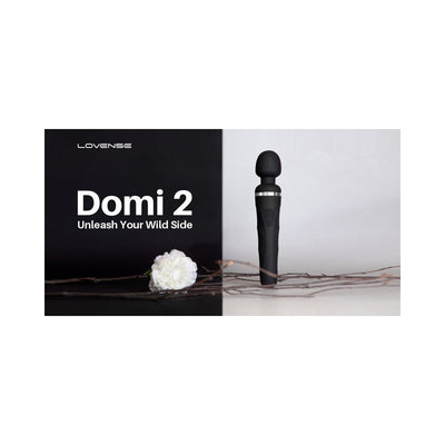 Lovense Domi 2 black wand vibrator standing upright with white flower and branches on a split black and white background.