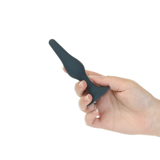 Hand holding a sleek black silicone tapered anal plug with a flared base against a white background.