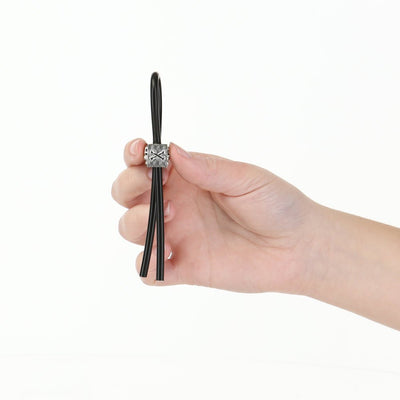 Hand holding a black adjustable silicone cock tie with a silver ABS slider against a white background.