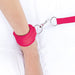 Close-up of a leg secured with a soft pink neoprene ankle cuff attached to a metal ring and strap on a white surface.