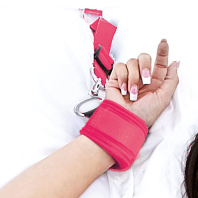 Close-up of a wrist secured in a vibrant pink adjustable cuff attached to a bed restraint system on white bedding.