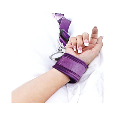 Close-up of a wrist secured in a purple adjustable strap cuff on white bedding.