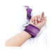 Close-up of a wrist secured in a purple adjustable strap cuff on white bedding.