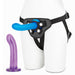 Adjustable black harness with blue strap-on dildo worn on mannequin, accompanied by a purple curved dildo with flared base.