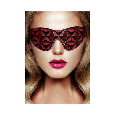 Close-up of a woman wearing a burgundy luxury eye mask with a geometric diamond pattern and an elastic band.