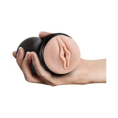 Hand holding a black cylindrical male pleasure toy with a realistic textured vaginal opening in vanilla color.