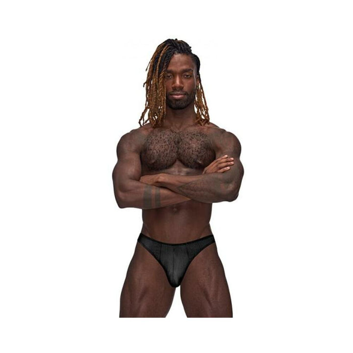 Muscular man wearing black Male Power Barely There Moonshine jock brief with subtle vertical stripes, standing with arms crossed.
