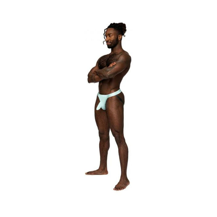 Male model wearing aqua Male Power Easy Breezy jock sleeve with satin elastic waistband and legbands, standing with arms crossed.