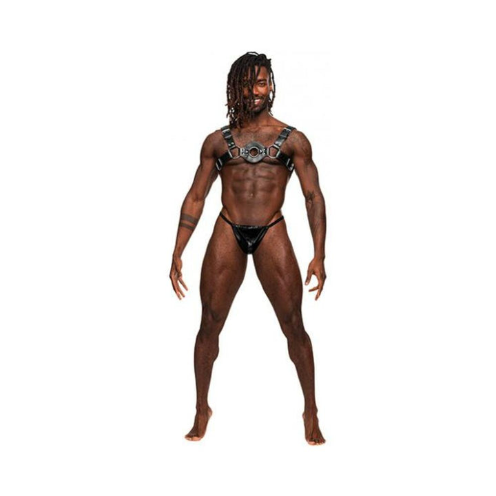 Muscular man wearing Male Power black leather chest harness with metal rings and black thong underwear on white background.