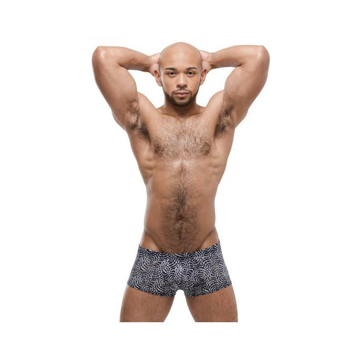 Muscular man wearing navy blue Male Power Mesmerizing Mini Shorts with swirling two-toned pattern posing with hands behind head.