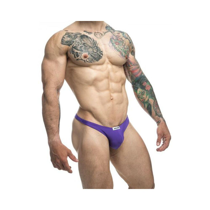 Muscular male model wearing purple Malebasics Justin + Simon classic tanga underwear with tattooed arms.