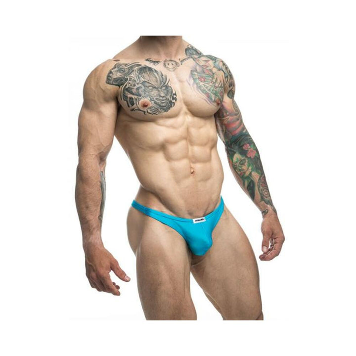 Muscular male model wearing turquoise Malebasics Justin + Simon classic tanga underwear with tattoos on arms and chest.