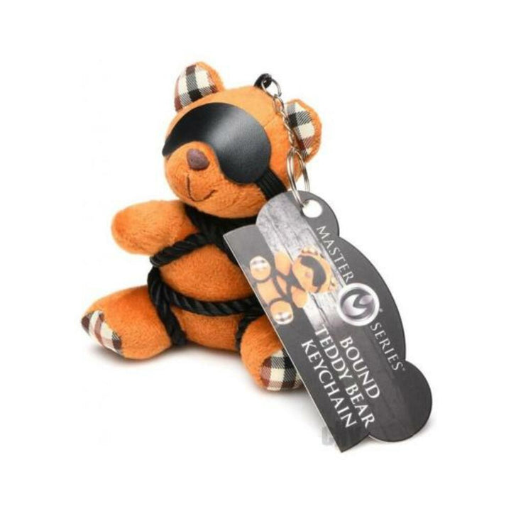 Small orange teddy bear keychain with plaid ear details, tied with black rope and wearing a removable black blindfold.