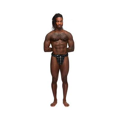 Athletic man wearing black leather thong with studded cage pouch and chastity lock, standing against white background.