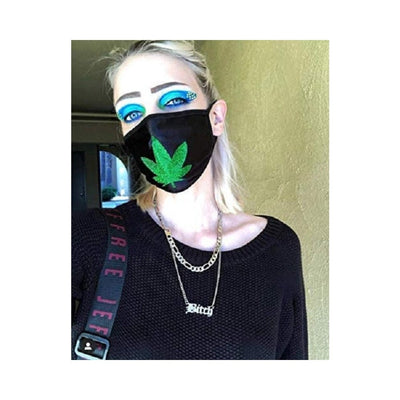 Person wearing black face mask with green glitter weed leaf design and black trim, paired with bold blue eye makeup and black sweater