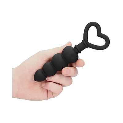 Hand holding black silicone anal beads with graduated rounded shapes and heart-shaped handle.