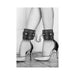 Black and white plush bonded leather ankle cuffs with chain connection worn with high heel shoes on wooden floor