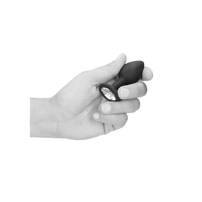 Hand holding a black silicone butt plug with a removable clear jewel at the base against a white background.