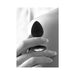 Black silicone butt plug with removable jewel held between fingers against skin background.