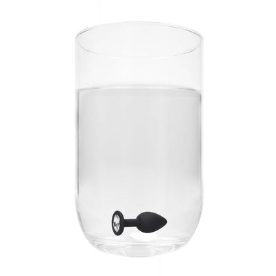 Black and white silicone butt plug with a removable clear jewel base submerged in a clear glass of water.