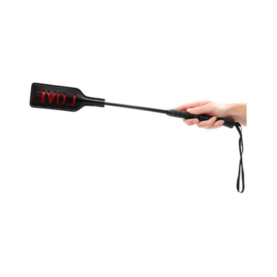 Hand holding a black short-handled crop with a rectangular tip featuring a red cutout of the word LOVE.