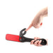 Black leather paddle with heart-shaped cutouts and red striking surface held and flexed by hands.