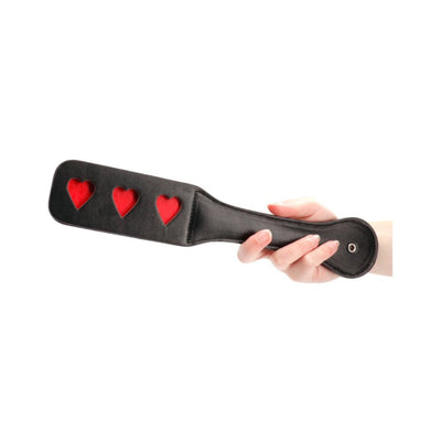 Hand holding black leather paddle with three red heart cutouts for playful imprinting.