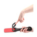 Black leather paddle with red striking surface and three lip-shaped cutouts, held and flexed by hands.
