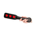 Hand holding black leather paddle with three red lips cut-out designs on the striking paddle surface.