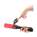 Black leather paddle with red striking surface and star-shaped cutout, held and flexed by hands on white background.