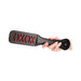 Hand holding black leather paddle with red "XOXO" cutout design and stitched edges against white background.