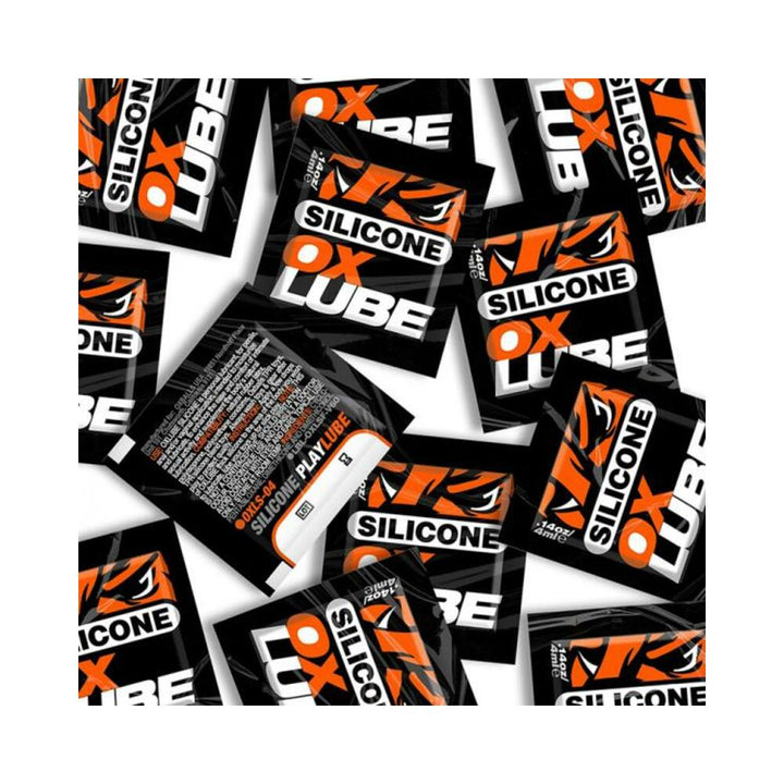 Multiple black and orange Oxballs Silicone Oxlube single-use packets scattered on a white background.