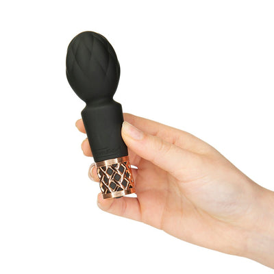 Hand holding a compact black silicone clitoral vibrator wand with a quilted head and rose gold lattice base.
