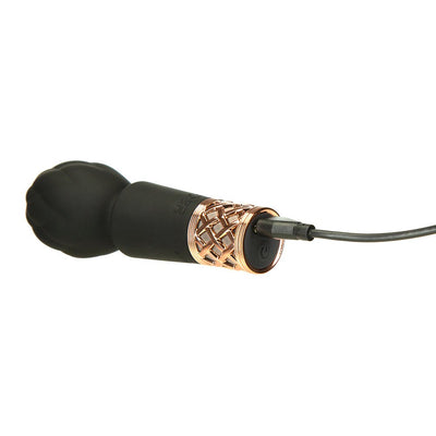 Compact black clitoral vibrator wand with quilted rose gold handle detail, shown charging with USB cable.