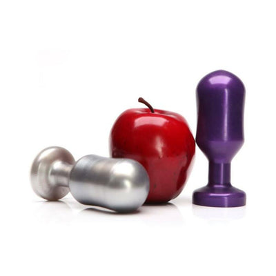 Two metal keg-shaped plugs in silver and midnight purple next to a red apple for size comparison on white background.