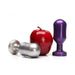 Two metal keg-shaped plugs in silver and midnight purple next to a red apple for size comparison on white background.