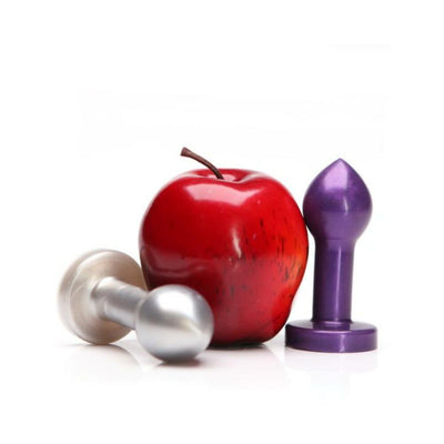 Two metal butt plugs, one silver and one purple, displayed next to a red apple on a white background.
