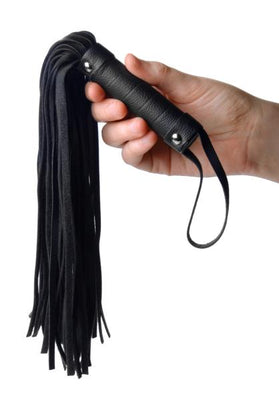 Hand holding a compact black pleather mini flogger with a studded handle and wrist loop.