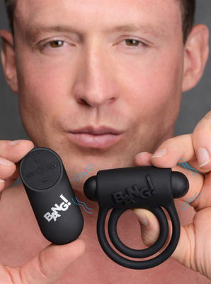Man holding black Bang! vibrating cock ring and remote control against gray background
