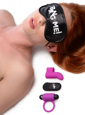 Woman wearing a black satin blindfold with "BANG ME!" text, next to a purple finger vibe, remote, and cock ring on white background.