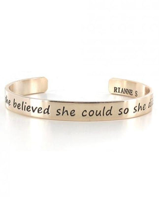 Gold-tone metal cuff bracelet engraved with the phrase she believed she could so she did and Rianne S branding inside.