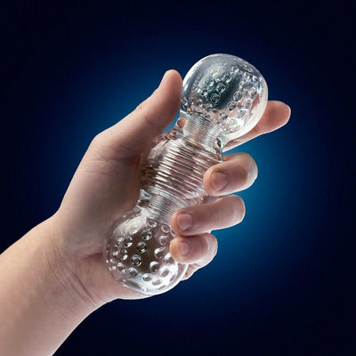 Hand holding a clear textured pleasure toy with ribbed and nodular chambers against a dark blue background.