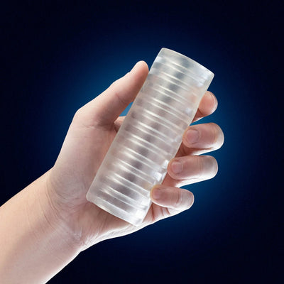 Hand holding a clear, ribbed, cylindrical stroker with a soft, textured surface against a dark blue background.