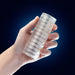 Hand holding a clear, ribbed, cylindrical stroker with a soft, textured surface against a dark blue background.