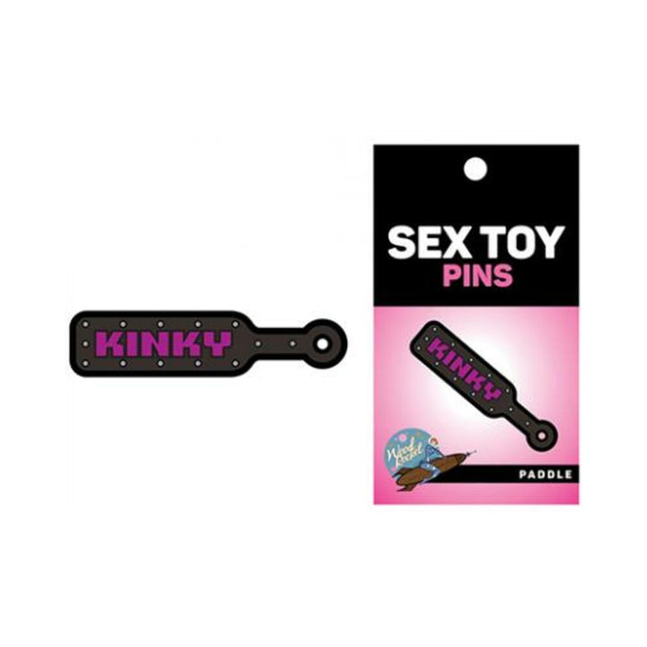Black enamel pin shaped like a paddle with the word kinky in pink, displayed on branded packaging.