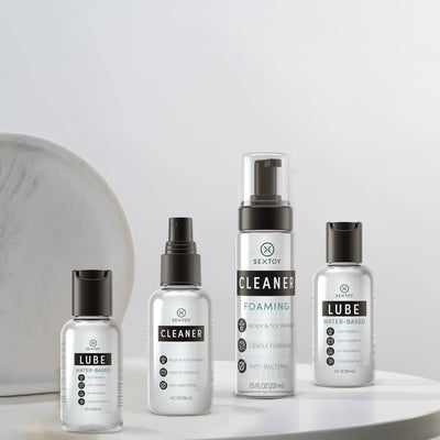 Four clear bottles of Sextoy brand intimate care products including water-based lube and foaming and spray cleaners on a white surface.