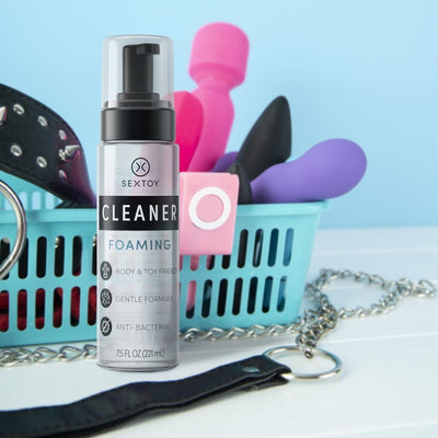 Sextoy Body & Toy Foaming Cleaner 7.5 oz bottle with assorted intimate accessories in a blue basket on a white surface.