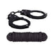 Black metal handcuffs with keys paired with a neatly coiled black soft cotton rope.